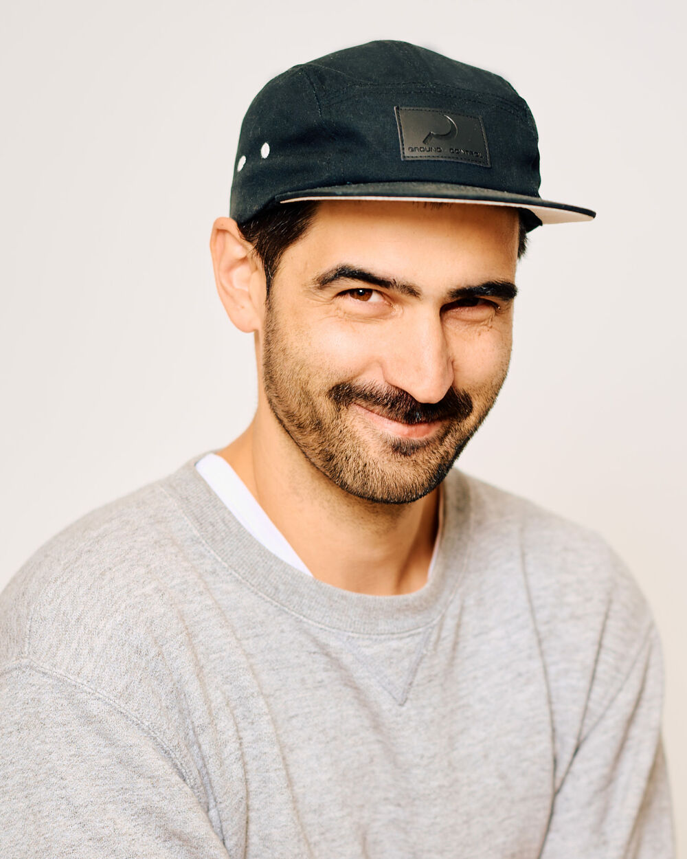 Unser Fotograf Nathan Dressen lacht verschmitzt in die Kamera. Er ist ein Mann in einem grauen Pullover und einem schwarzen Cappie. 